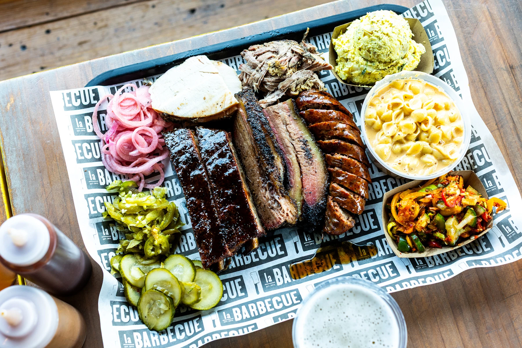 La Barbecue signature dishes Beef Brisket, Pork Ribs, El Sancho Loco Sandwich (pulled pork, sausage, pickled onions), Beef Ribs (on specific days).